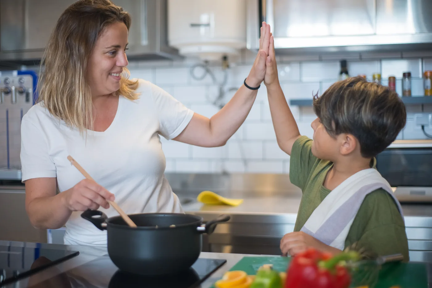A nanny and a boy high-fiving while cooking together