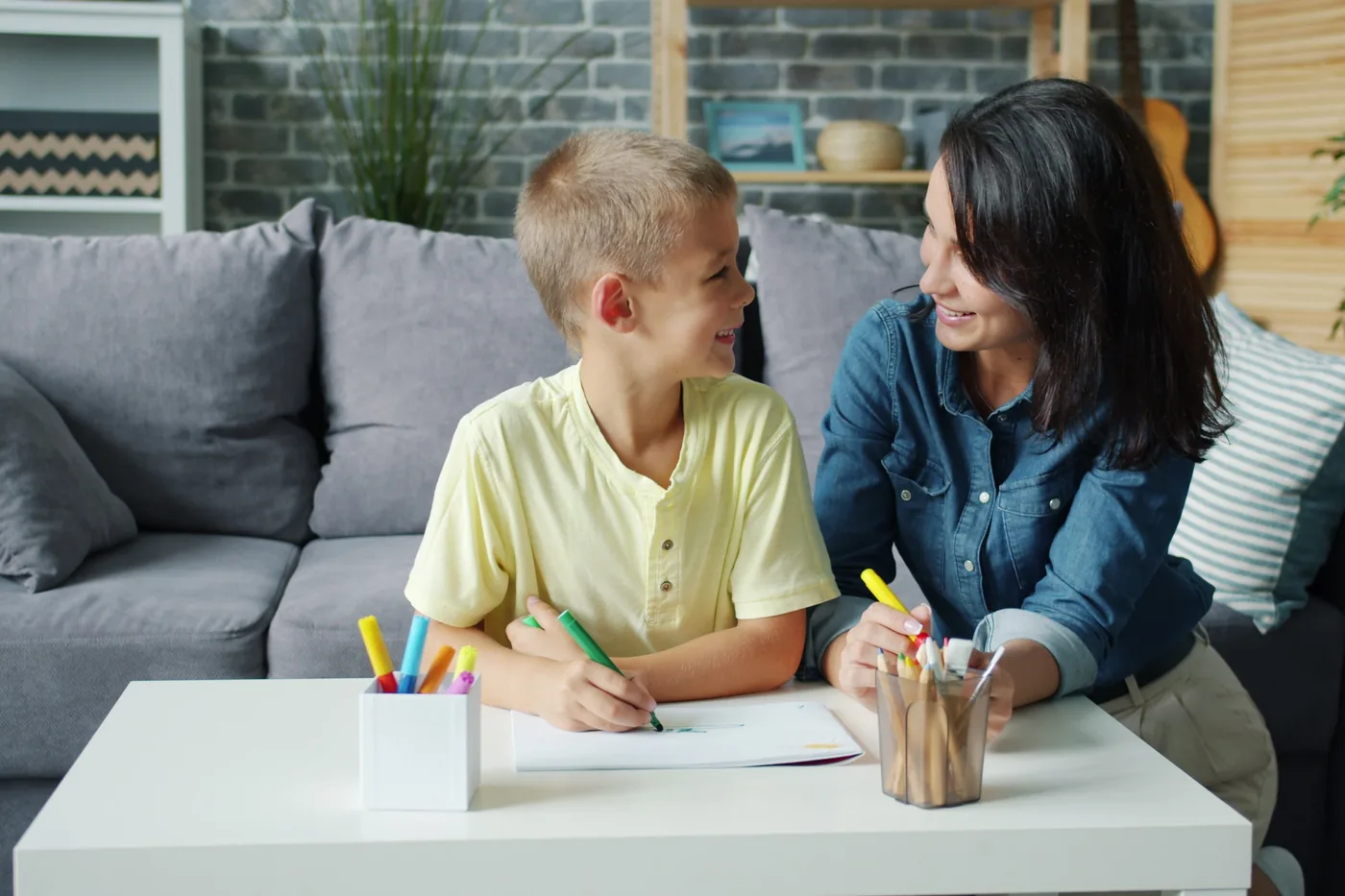 A nanny drawing at the table with a young boy
